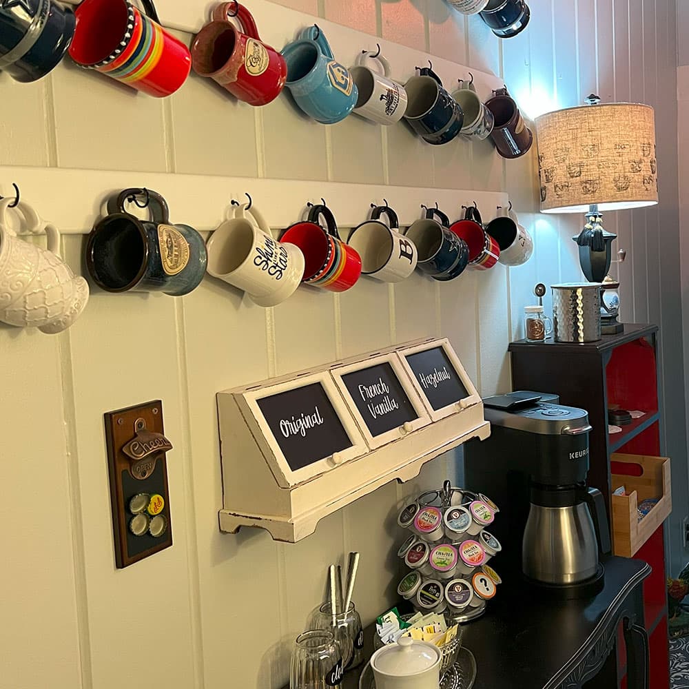 A wall-mounted display features various mugs and a coffee station with K-Cups, accompanied by a lamp.