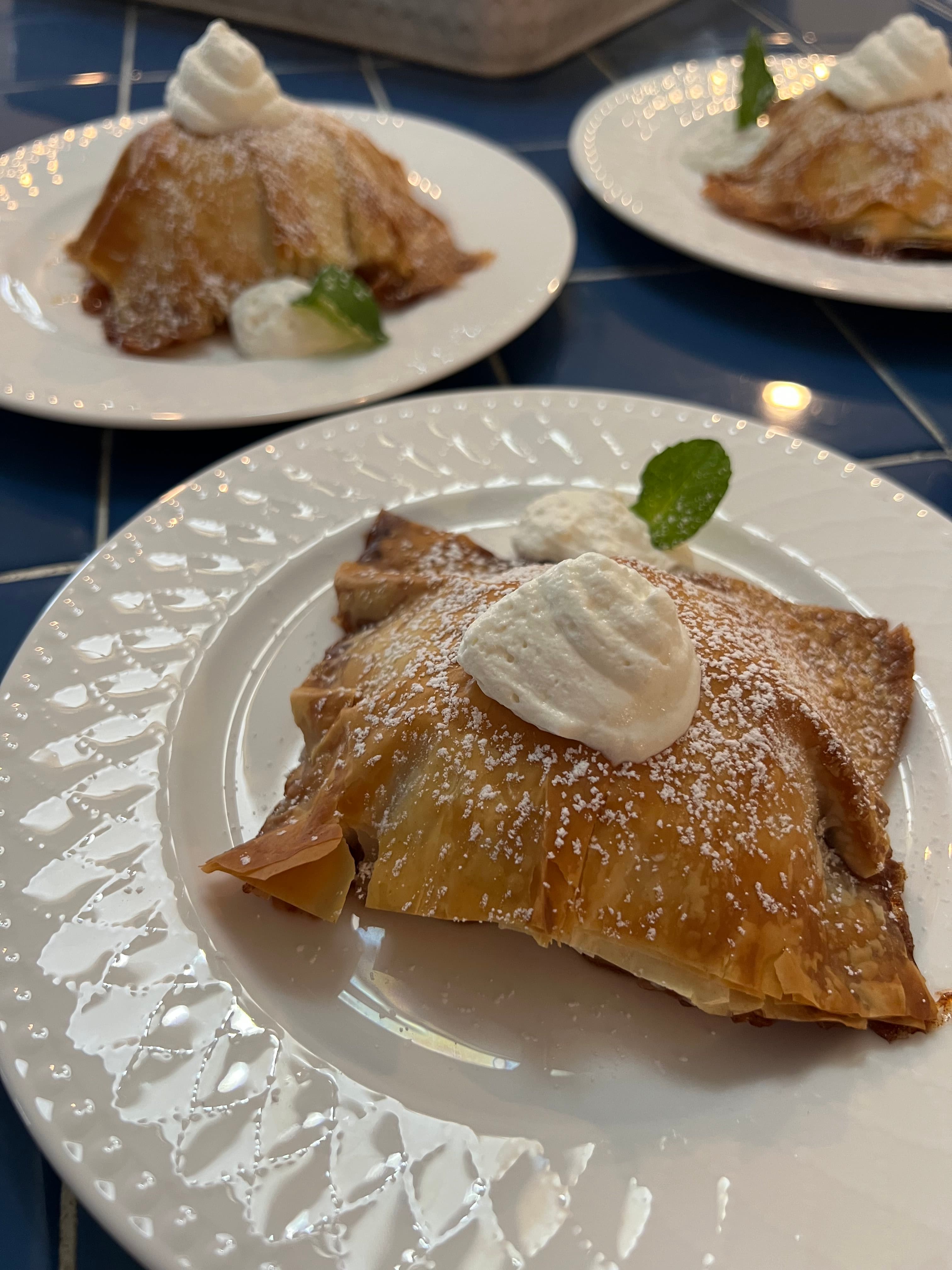Plated pastry dessert topped with whipped cream and mint leaves, garnished with powdered sugar.