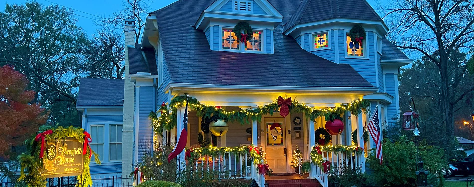 A beautifully decorated blue house illuminated with holiday lights and garlands.