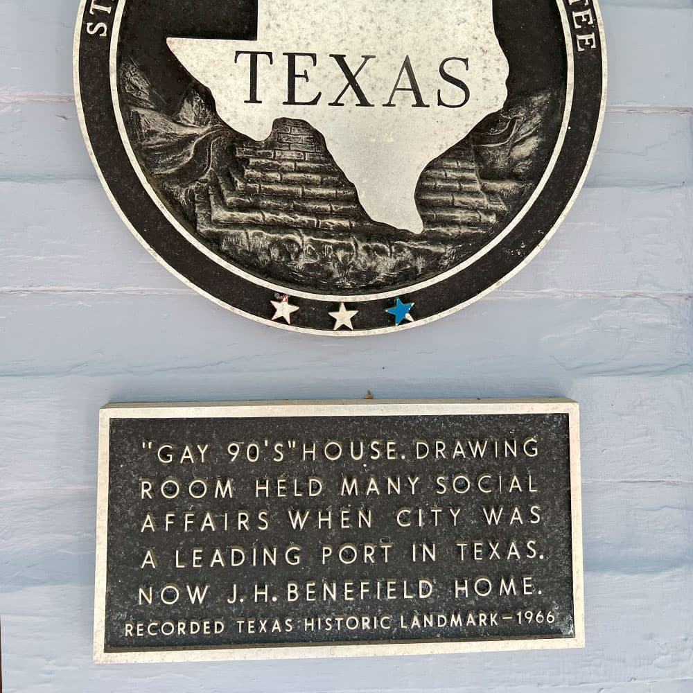 A plaque detailing the history of the "Gay 90's House" in Texas, noting its significance as a former social venue and current historical landmark.