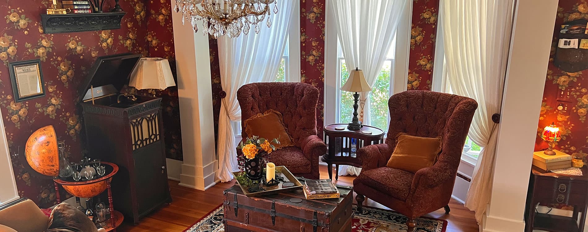 A cozy living room with two armchairs, a vintage record player, and floral wallpaper.