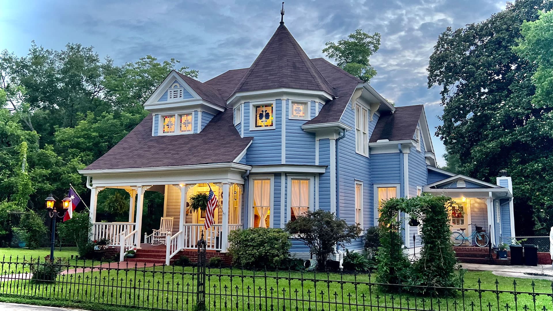 A charming blue Victorian house with a turret and a welcoming porch set in a green landscape.