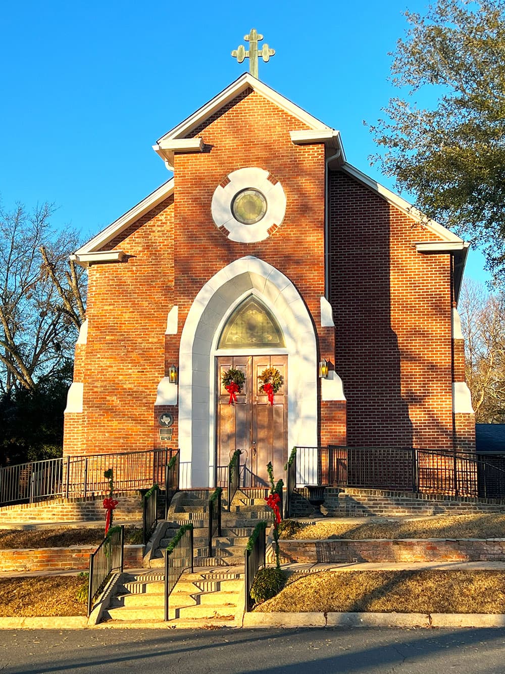 A brick church adorned with holiday wreaths and a cross on top, set against a clear blue sky.